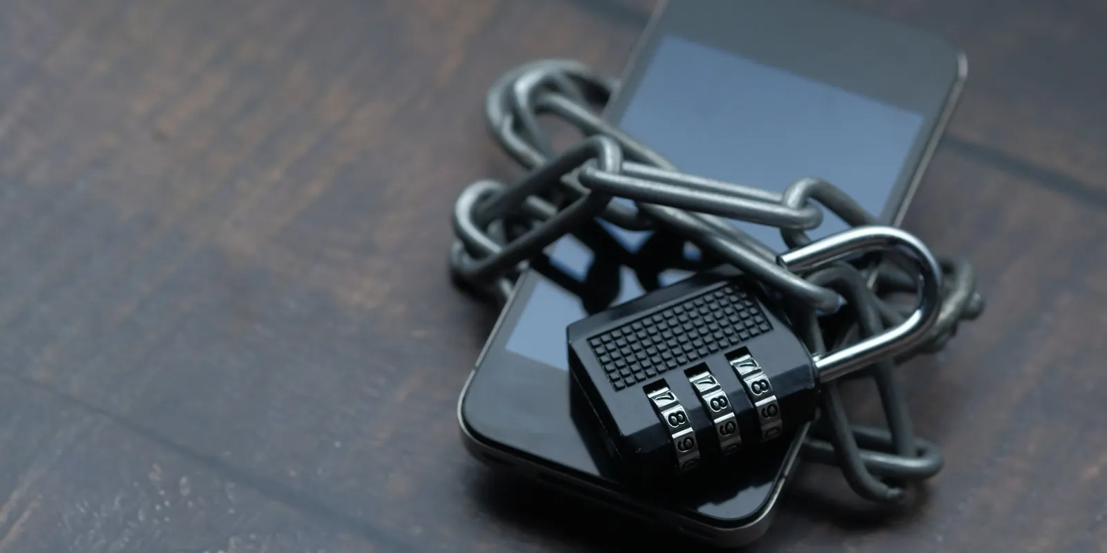 A smartphone wrapped in a chain and fastened with a combination padlock