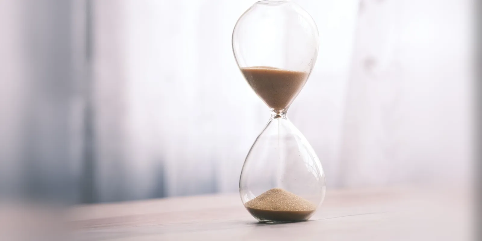 Hourglass with sand running on a wooden table in soft window light